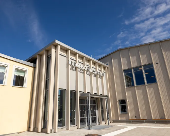 En stor skolbyggnad med många fönster och en himmel som bakgrund.